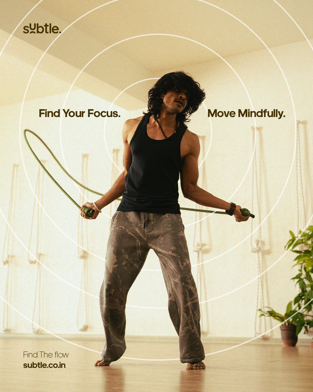 A man in a black tank top and patterned pants holds a jump rope in a bright indoor studio with text overlays reading 'Find Your Focus. Move Mindfully.